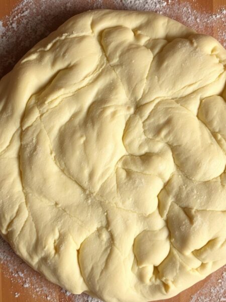 A perfectly round, golden-brown pizza dough with a soft, airy interior and a delicate, chewy crust. The dough is dusted with a light coating of fine flour, creating a subtle texture. Captured in a warm, natural lighting that accentuates the dough's supple structure and subtle sheen. Photographed from an overhead angle, showcasing the dough's authenticity and the process of hand-stretching it into a classic Neapolitan pizza shape. The image exudes the comforting aromas and rustic charm of an authentic Italian kitchen, inviting the viewer to imagine the delicious pizza that will soon emerge from the oven.